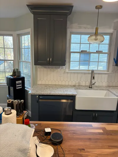 Charcoal kitchen cabinets, white farmhouse sink, granite counters and picket tile backsplash beneath a window.