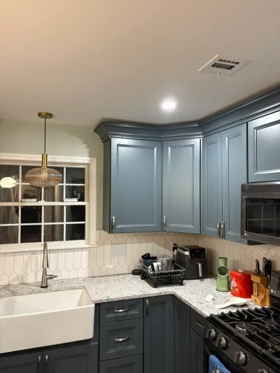 Kitchen with slate blue raised-panel cabinets, granite counters, farmhouse sink and picket tile backsplash.