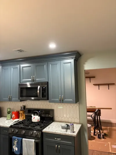 Blue-gray kitchen cabinets, granite counters and picket tile backsplash beside a room still under renovation.