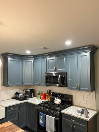 L-shaped kitchen with blue-gray upper cabinets, charcoal base cabinets, granite counters and picket tile backsplash.