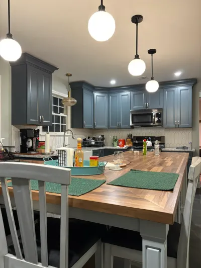 Blue-gray shaker kitchen with butcher block island table, globe pendants, white tile backsplash and stainless appliances.