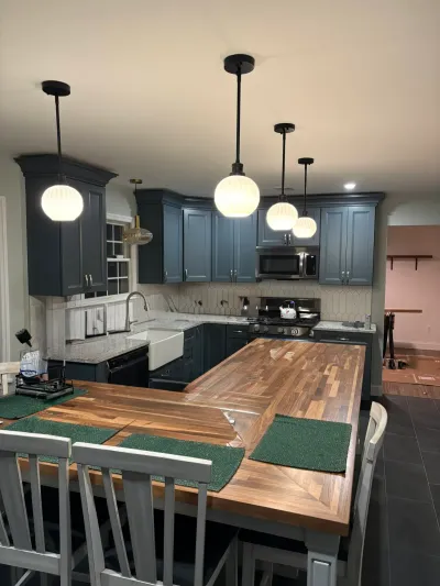 Kitchen with dark blue cabinets, butcher block peninsula, farmhouse sink and black globe pendant lights.