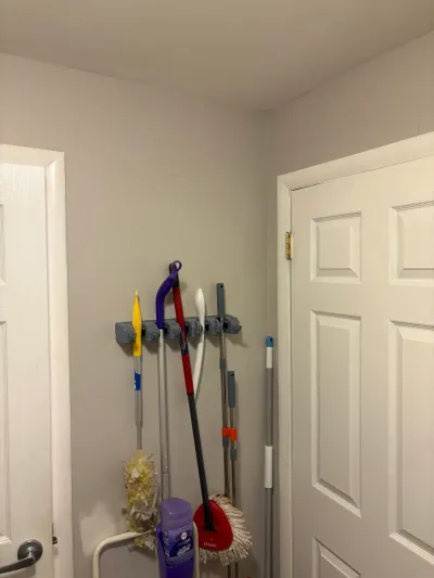 Corner of a utility closet with brooms and mops on a wall rack between two white panel doors.