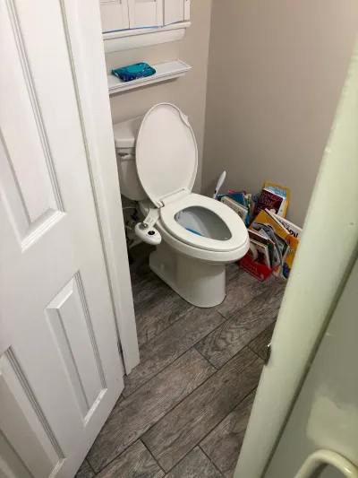 Small bathroom toilet alcove with bidet seat, wall shelf, gray wood-look tile floor and stacked books