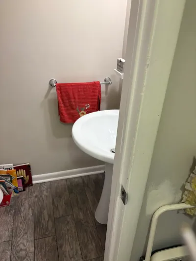 Small bathroom with white pedestal sink, red towel on chrome bar, and wood-look tile floor.