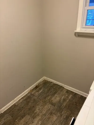 Empty bathroom corner with gray walls, white baseboard, wood-look tile floor and a small window