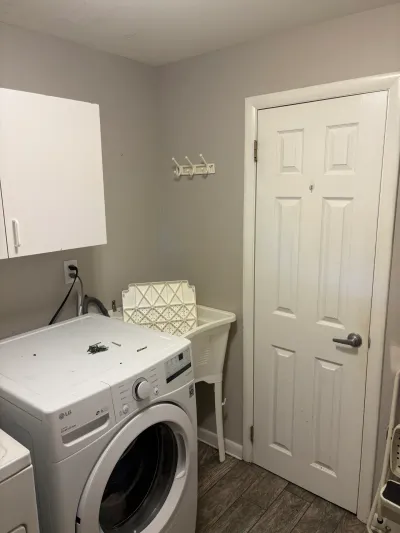 Small laundry room with white front-load washer, upper cabinet, utility sink and six-panel door