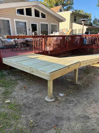 New pressure-treated deck platform on concrete pier footings built alongside an existing red-stained deck.