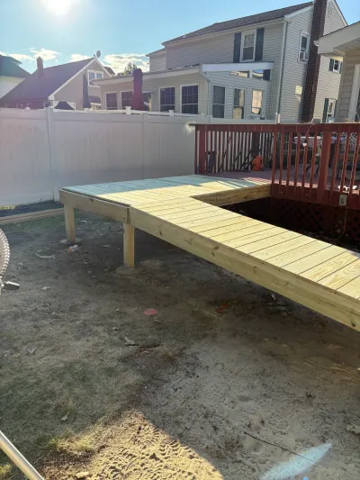 New pressure-treated ground-level deck under construction beside an existing stained raised deck.
