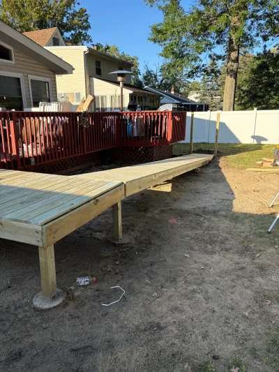 New pressure-treated deck platform and walkway under construction connecting to an existing red deck.