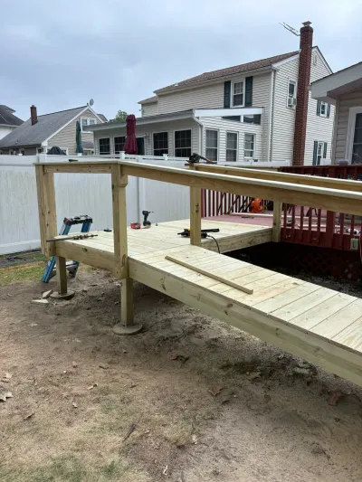 Partially built pressure-treated wood deck with rail posts and tools, next to an existing red deck.