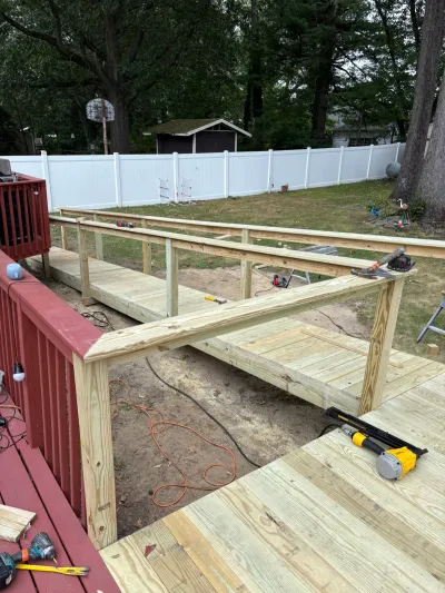 New pressure-treated deck under construction with railing posts installed, tools nearby, white vinyl fence beyond.