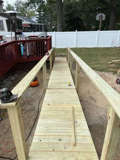 Newly framed pressure-treated wood ramp with guardrails leading from a red deck across a sandy backyard.