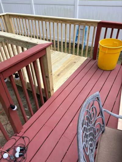 Deck under renovation with new natural wood railing joining an existing red-painted deck and railing.