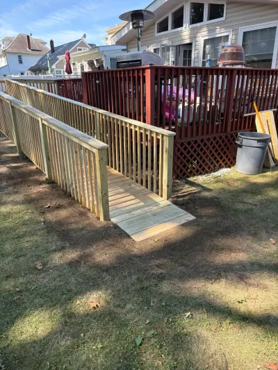 New pressure-treated wheelchair ramp with railings leading down from a stained backyard deck to the lawn.
