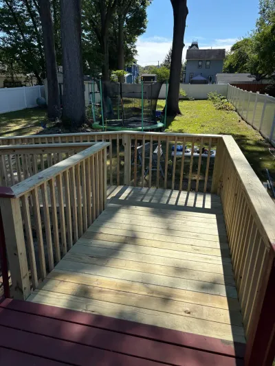 Newly framed pressure-treated deck with baluster railing stepping down from an existing burgundy-painted deck.