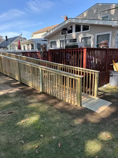 Newly built pressure-treated wheelchair ramp with picket railings leading to a red-stained backyard deck.','altText':'x