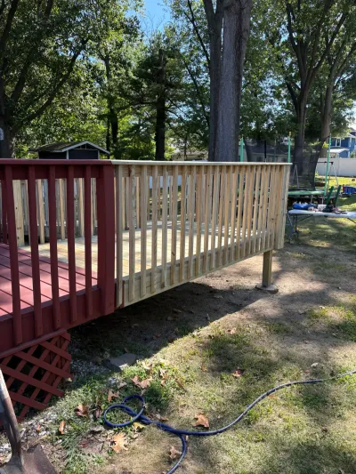 New pressure-treated deck extension with wood railing joined to an existing red-painted backyard deck.