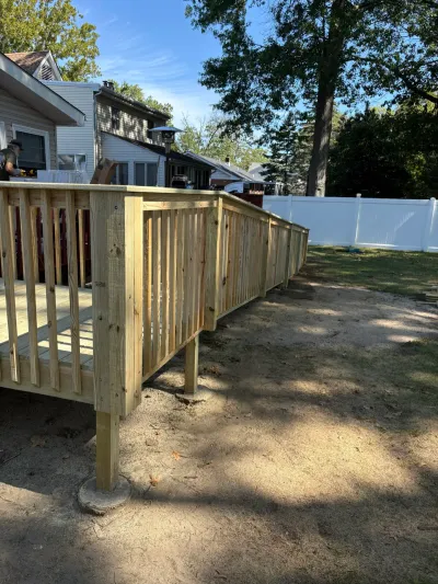 New pressure-treated wood deck with baluster railing under construction behind a vinyl-sided house.
