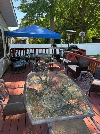 Weathered red-stained backyard wood deck with patio furniture, blue canopy tent and white vinyl fence.