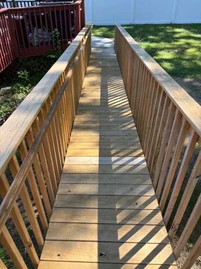 Wood accessible ramp with balusters and handrails descending from a red-stained deck to a grassy yard.