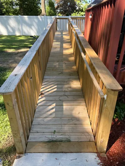 Newly built pressure-treated wood accessibility ramp with handrails leading up to a red-railed backyard deck.