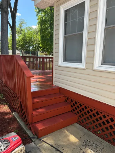 Freshly stained barn-red wood deck steps and lattice skirting beside a cream vinyl-sided house.
