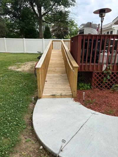 New pressure-treated wood accessibility ramp with handrails leading from a concrete pad up to a stained backyard deck.