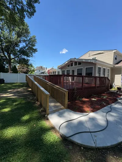 Backyard deck with red-brown railings and a new pressure-treated wheelchair ramp leading to a concrete patio.