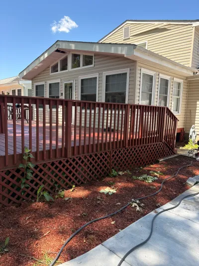 Raised red-stained wood deck with lattice skirting along the rear addition of a cream vinyl-sided house.