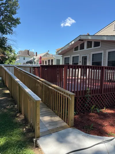 New pressure-treated wheelchair ramp with handrails leading to a red-stained backyard deck on a sunny day.