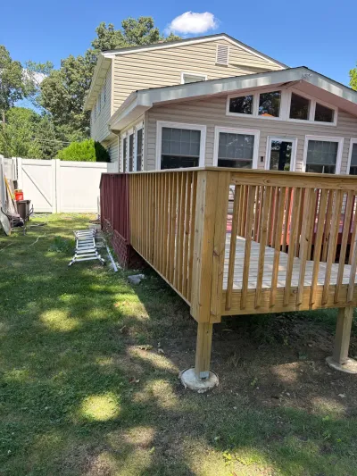 New pressure-treated wood deck on concrete piers under construction behind a vinyl-sided house.