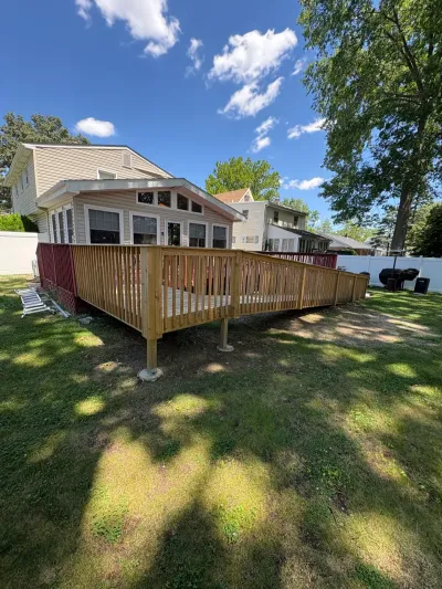 Newly built raised pressure-treated wood deck with baluster railing along the back of a beige two-story home.