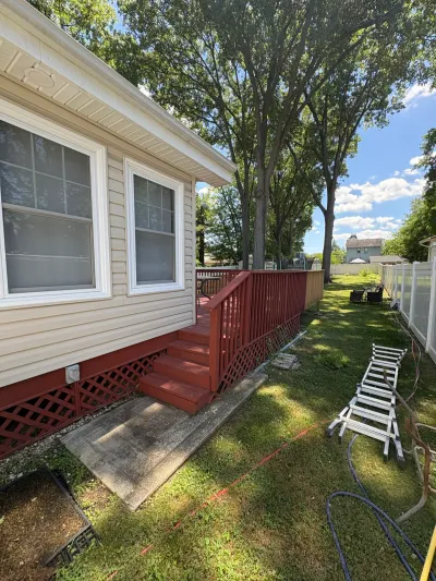 Cream vinyl-sided house with a red wood deck, stairs and lattice skirting beside a grassy fenced yard.