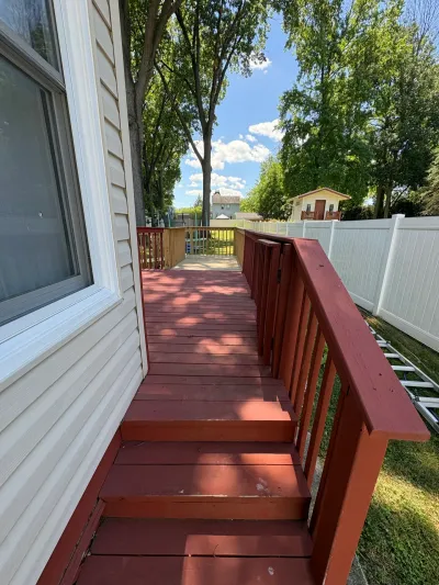 Red-brown stained wood deck with matching railing running alongside cream vinyl siding to a wide stair.