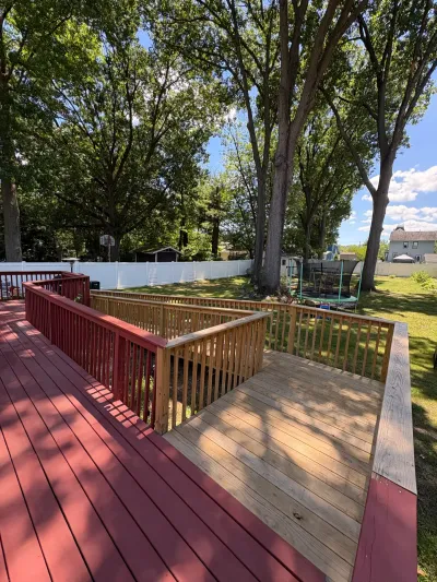 Backyard deck with a new bare pressure-treated section joined to an existing red-stained deck and railings.