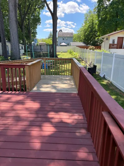 Two-level backyard wood deck, upper section stained red and lower landing left bare, overlooking a fenced lawn.