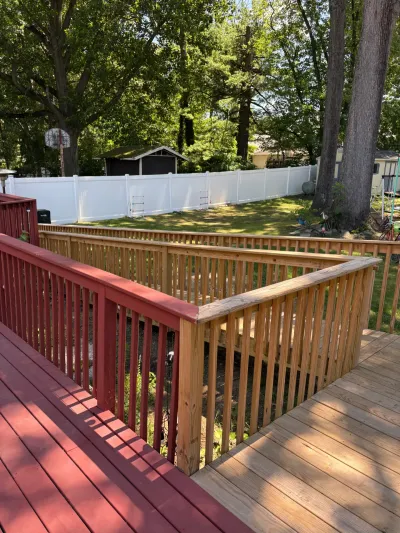 Backyard deck with new natural wood railing joining an older red-stained deck section, fenced yard beyond.