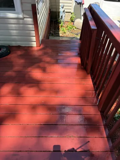 Freshly stained barn-red wood deck with matching railing, still wet, beside a white-sided house.