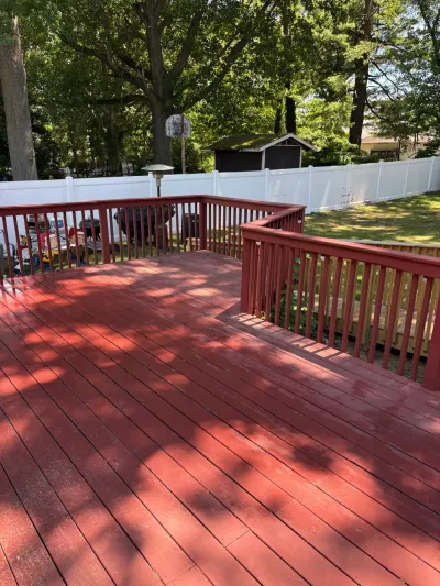 Freshly stained red backyard deck with matching railings, stepping down to a lower wood platform and lawn.