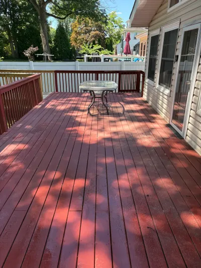 Raised backyard wood deck with faded red stain, red railings, patio table, and sliding glass door.