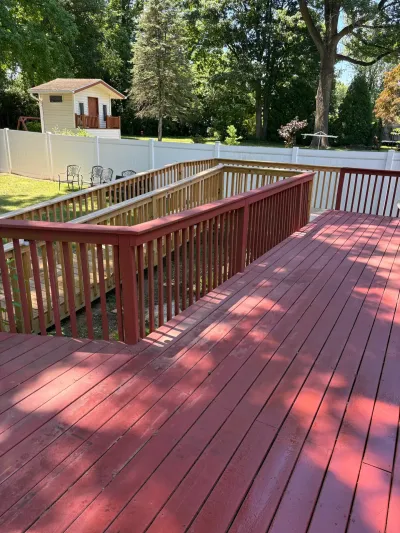 Red-stained backyard deck with a new tan wood access ramp and railing, white vinyl fence beyond.
