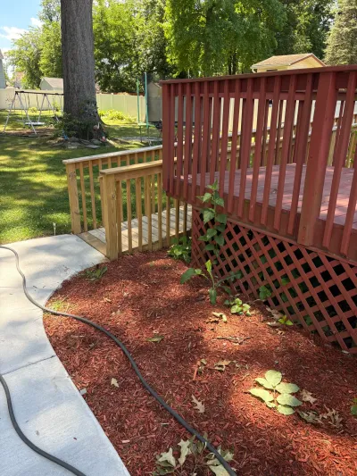 Red-stained backyard deck with lattice skirting and a new unstained wood ramp leading to a concrete walkway.