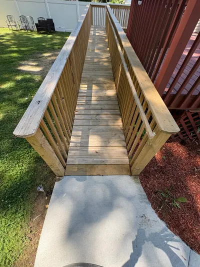 Finished pressure-treated wood accessibility ramp with balusters and handrails leading to a concrete pad.