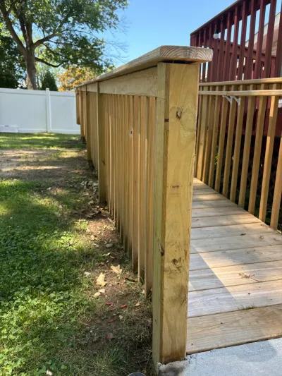 New pressure-treated wood ramp with baluster railings leading down from a red-stained deck to a concrete pad.