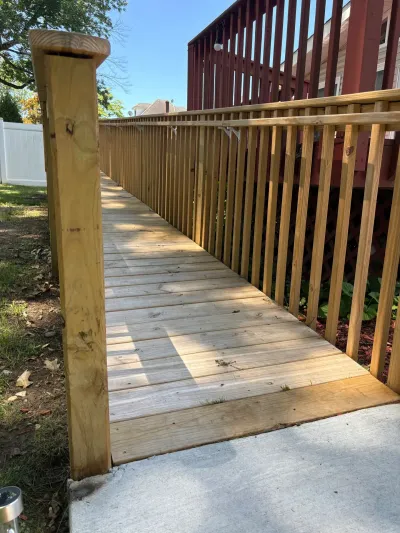 New pressure-treated wood wheelchair ramp with railings sloping down to a concrete walkway beside a deck.