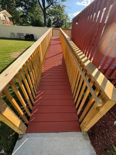 Red-stained wooden accessibility ramp with natural wood railings leading from a raised deck to a concrete pad.