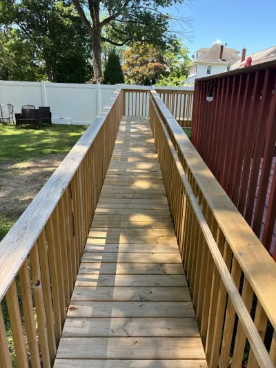 Pressure-treated wood access ramp with picket guardrails sloping down to a gate in a white vinyl fence.