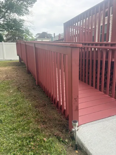 Barn-red painted wood deck with matching railed ramp sloping down to a concrete walkway beside a lawn.