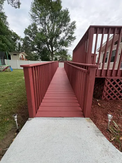 Red-stained wooden wheelchair ramp rising from a concrete pad to an elevated backyard deck.